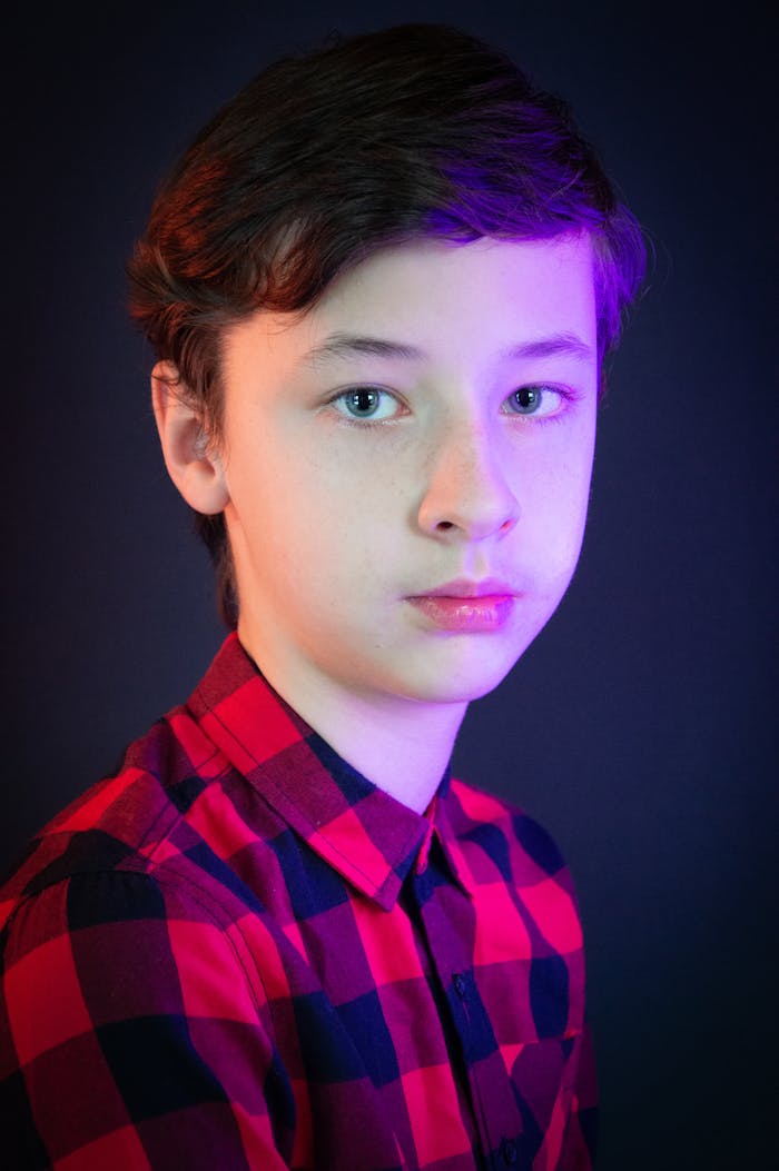 A young boy in a red checkered shirt with colorful studio lighting, looking directly at the camera.