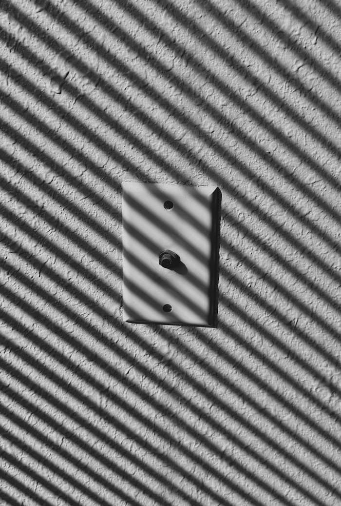 Black and white photo of a vintage TV antenna wall plate casting striped shadows on a textured wall.