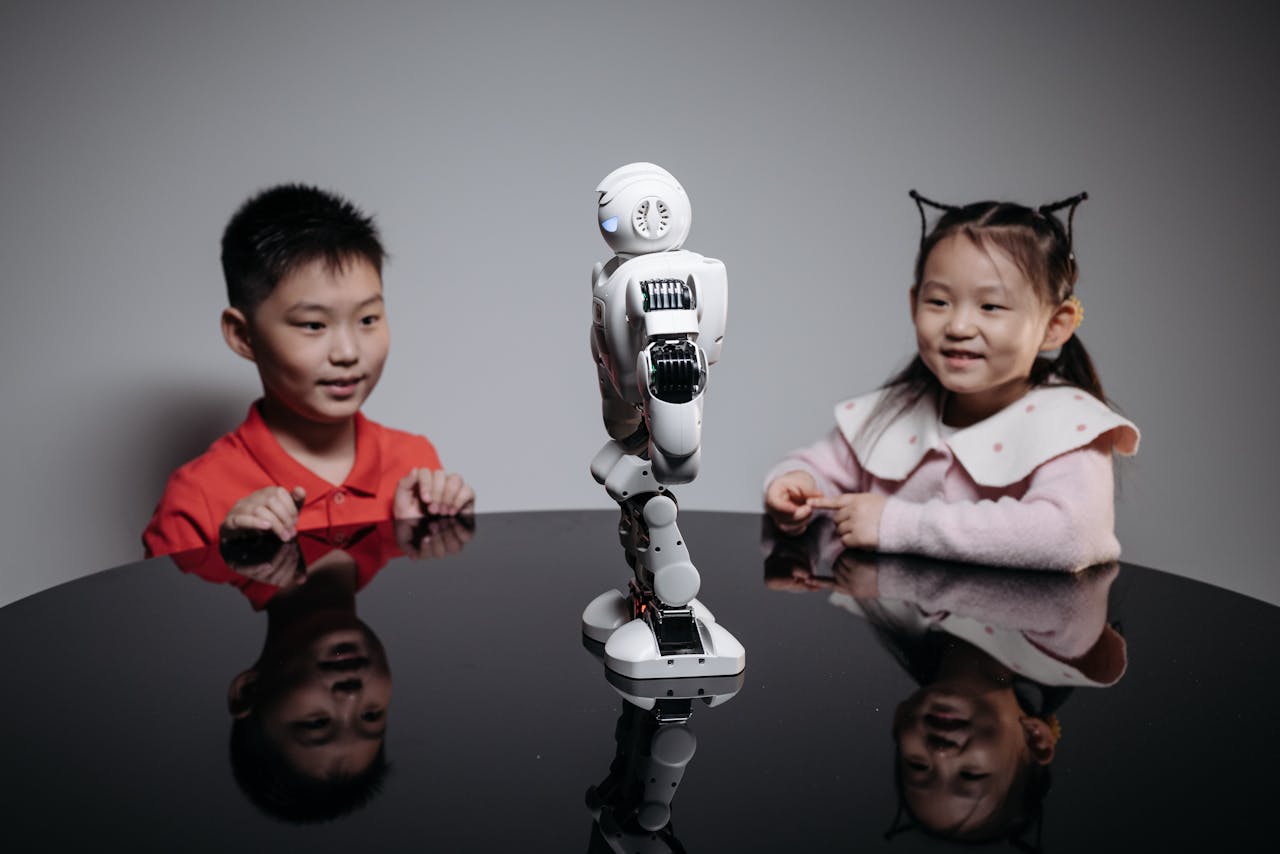 Two children fascinated by a small humanoid robot indoors on a table.